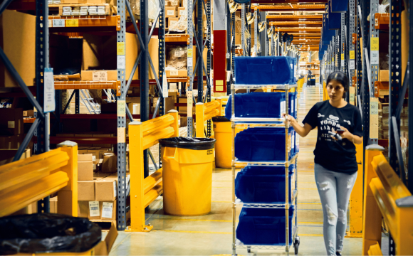 A ShipBob employee pushes a picking cart through a warehouse aisle as she fulfills orders. 